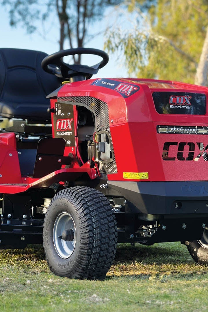 A Red Cox Ride-on mower parked sideways for display with blurred gumtrees in the back ground. 