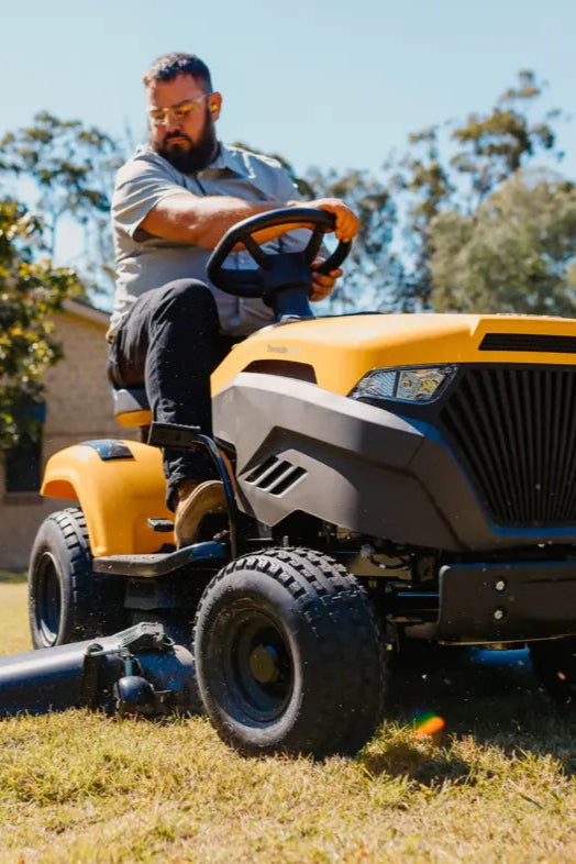 A yellow Stiga RIde-on mower being driven by a person mowing a lawn