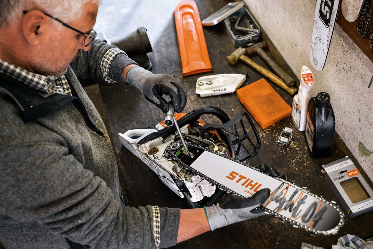 A person tightening a chainsaw chain on a Stihl chainsaw with Stihl tools on a wood workbench. 
