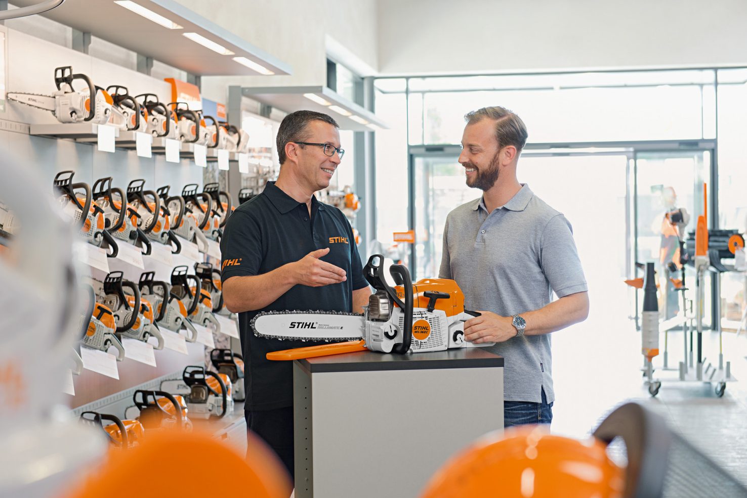 A sales person demonstrating a Stihl products to a customer in a Stihl showroom with chainsaws.